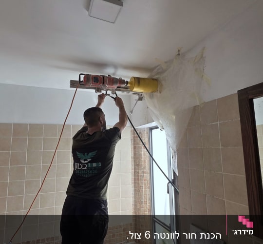 אדם קודח תקרה בחדר אמבטיה עם מקדחה